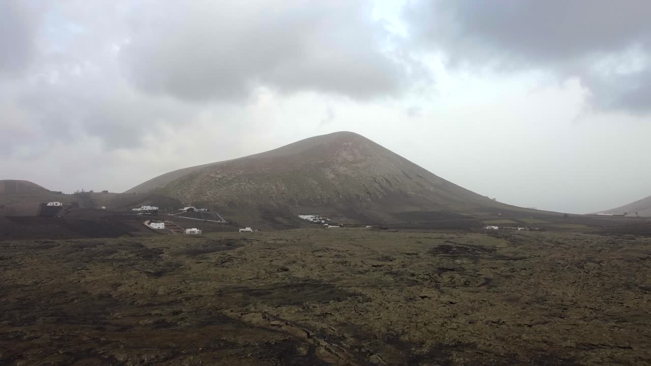 Drone shot of rocks and lava fields with volcano backdrop in Lanzarote