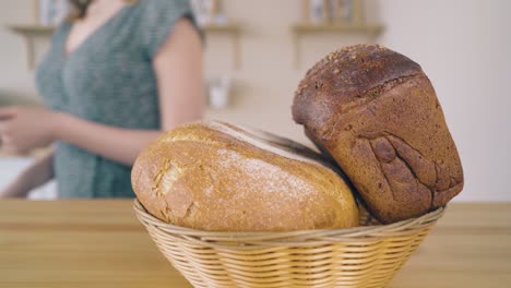 Frau-Stellt-Weidenkorb-Mit-Selbstgebackenem-Brot-Auf-Den-Tisch