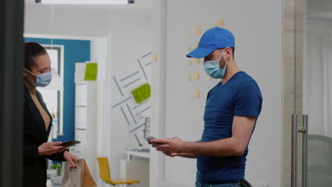 Businesswoman-with-face-mask-receiving-takeaway-food-lunch-order-paying-with-smartphone