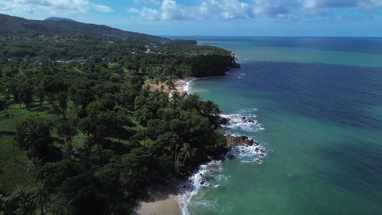 Aerial drone rising above lush palm trees on Koh Lanta, Thailand, revealing a hidden tropical beach and wide open turquoise ocean in the background with pristine coastal scenery