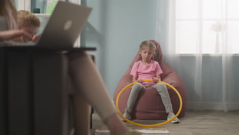 sad little girl sits in bean chair mother works on laptop