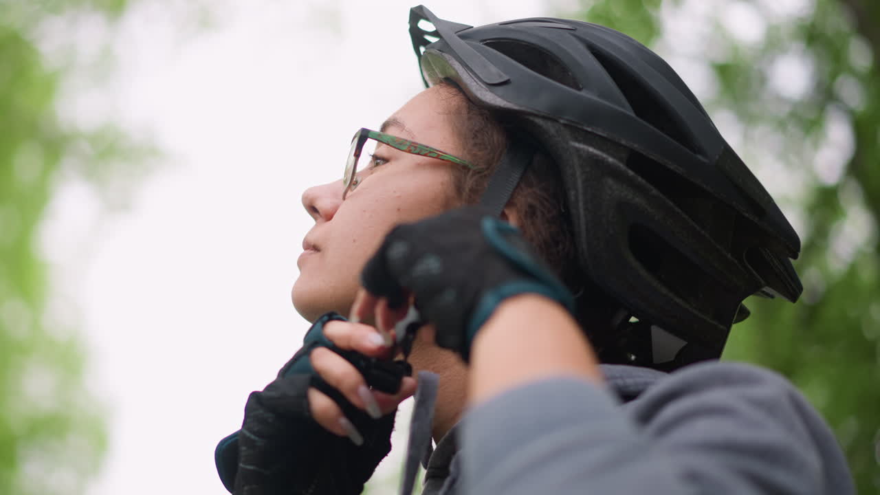 Focused Rider Secures Helmet Firmly, Calm Cyclist Adjusts Helmet Beneath Trees, Cyclist Secures His Helmet With Confidence While Surrounded By Vibrant Green Foliage And Peaceful Nature