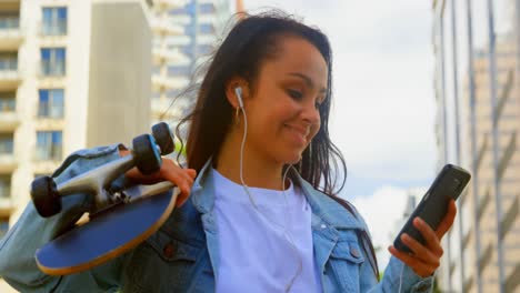 Mujer-Joven-Sosteniendo-Patineta-Mientras-Usa-El-Teléfono-Móvil-En-La-Ciudad-4k