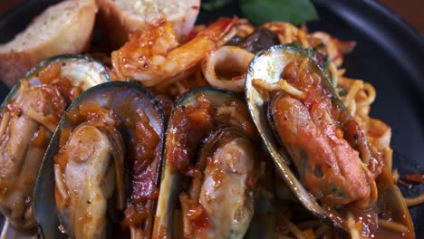 spaghetti with freshly cooked muscles and garlic bread spinning on a black plate close up