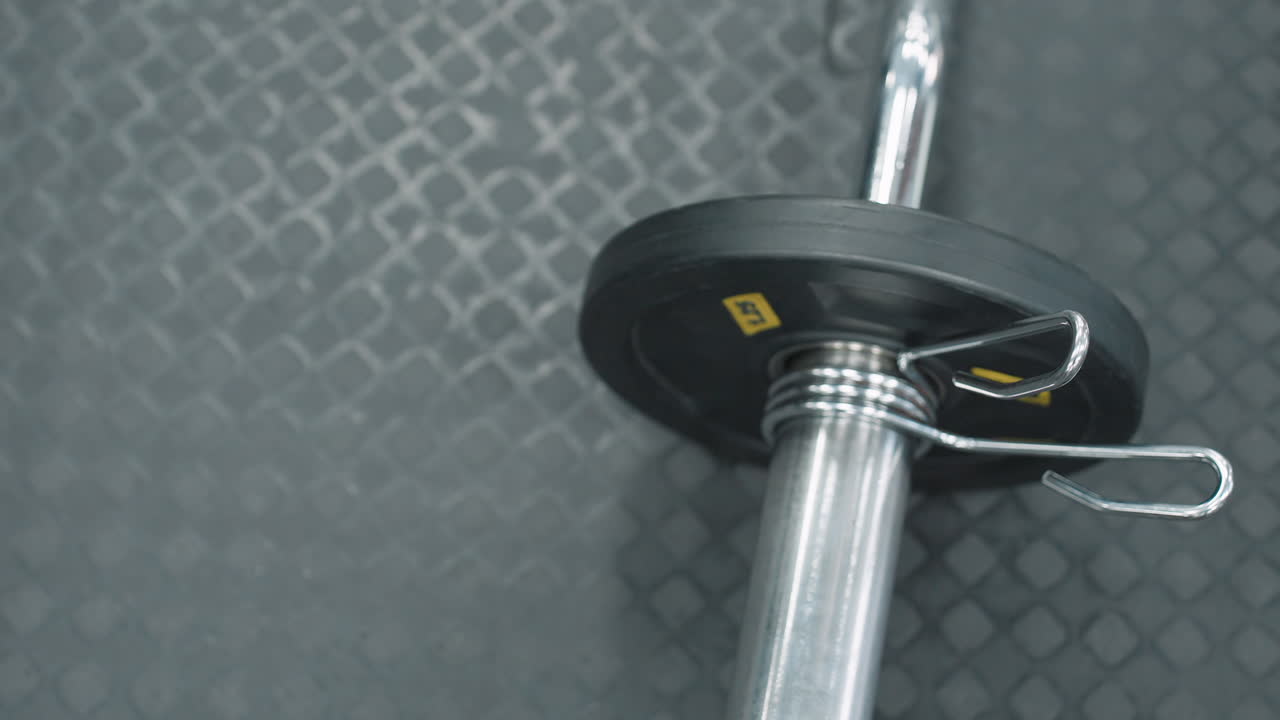 Close up top down view of athlete hands clipping weight plate onto barbell sleeve on rubber gym floor with white sneakers and metal spring collar visible during intense workout preparation