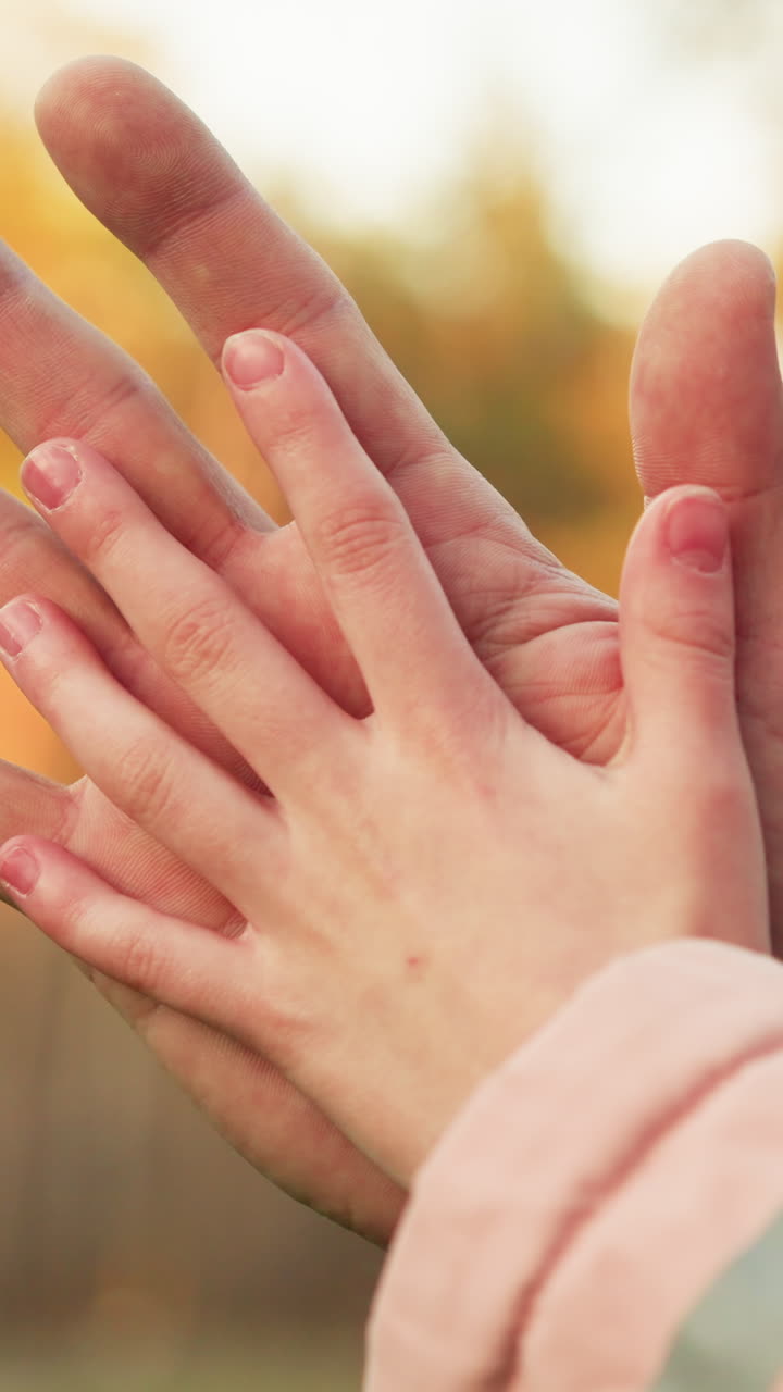 클로즈업은 따뜻하고 흐릿한 가을 배경에 어른의 손이 아동의 손에 부드럽게 앉아있는 부드러운 순간을 포착합니다.