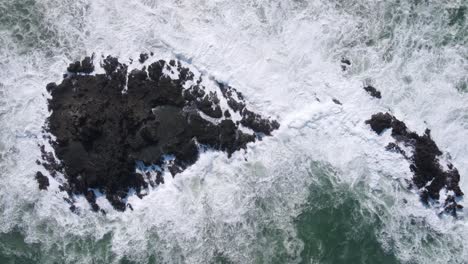 Top-down-view-of-waves-breaking-into-coral-rock-on-the-sea-and-produce-white-foam