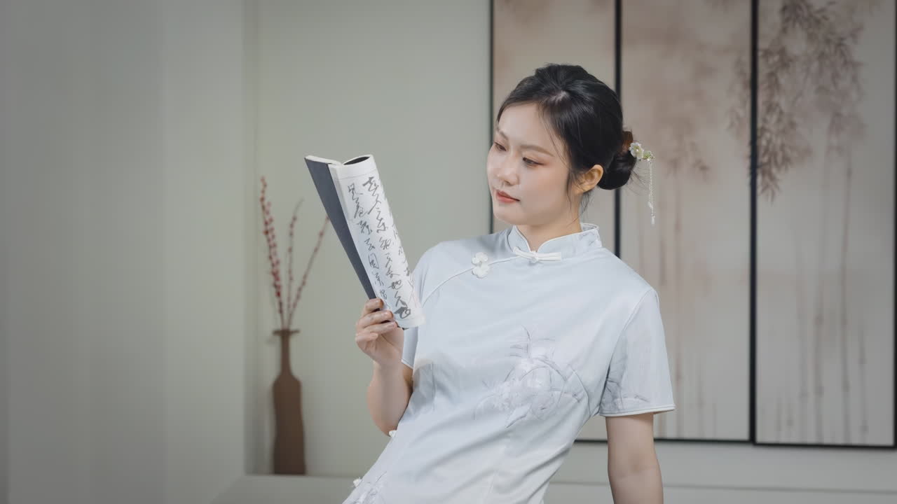 レトロで美しい伝統的なチャイナドレスを着た若い女性が、集中して本を読んでいる。中国の歴史文化を楽しみ、自宅で紅茶を飲みながら勉強し、良い週末を過ごす様子。