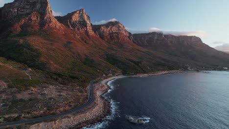 Vista-Aérea-Sobre-La-Carretera-Costera-Con-La-Montaña-De-Los-Doce-Apóstoles-En-Ciudad-Del-Cabo,-Sudáfrica---Disparo-De-Drones