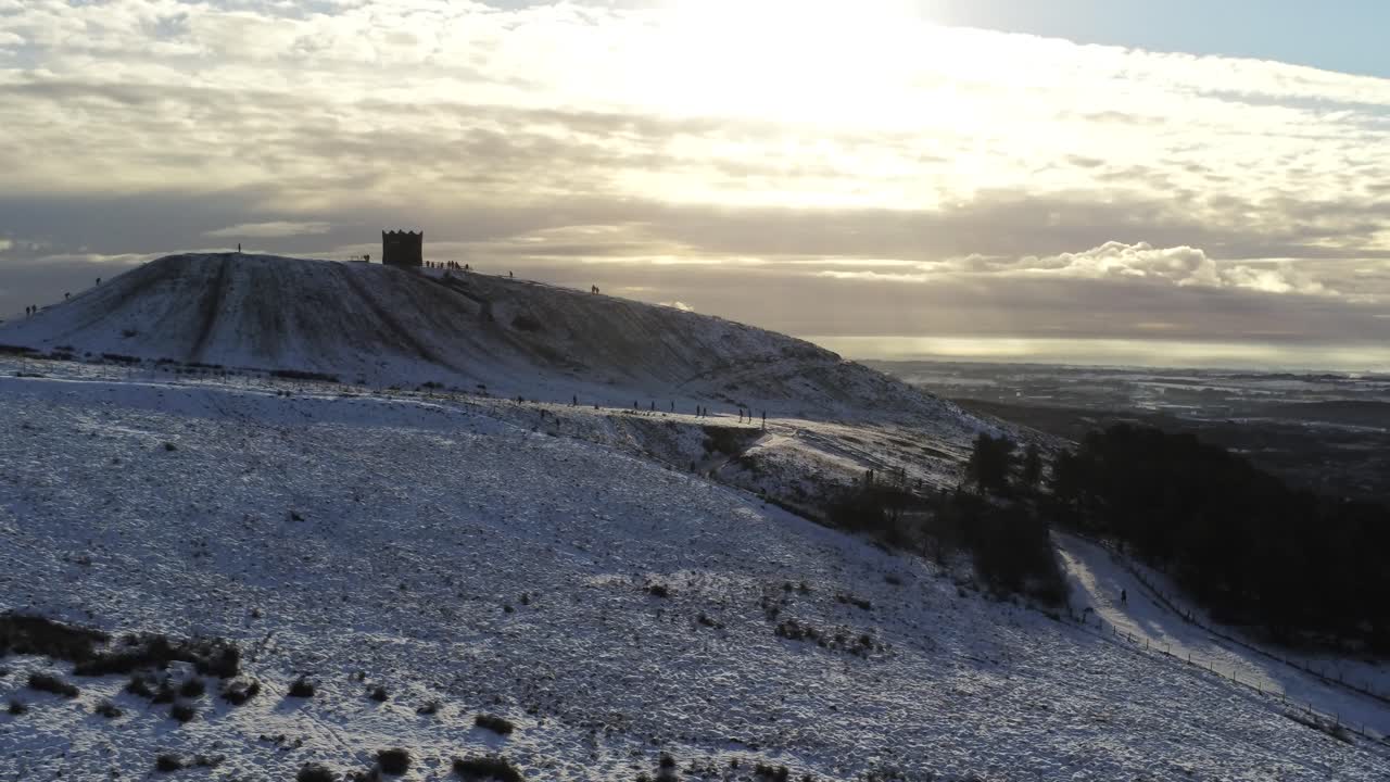 snowy rivington pike tower winter hill vista aérea gente en trineo cuesta abajo al amanecer orbita ascendente izquierda al amanecer