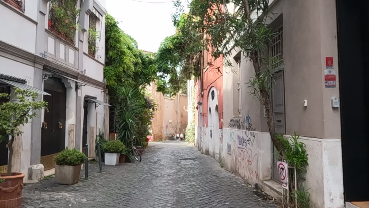 Tranquilla via stretta fiancheggiata da architettura tradizionale, edera verde lussureggiante e lastricato in ciottoli in un quartiere storico romano. Autentico paesaggio urbano italiano ricco di carattere.