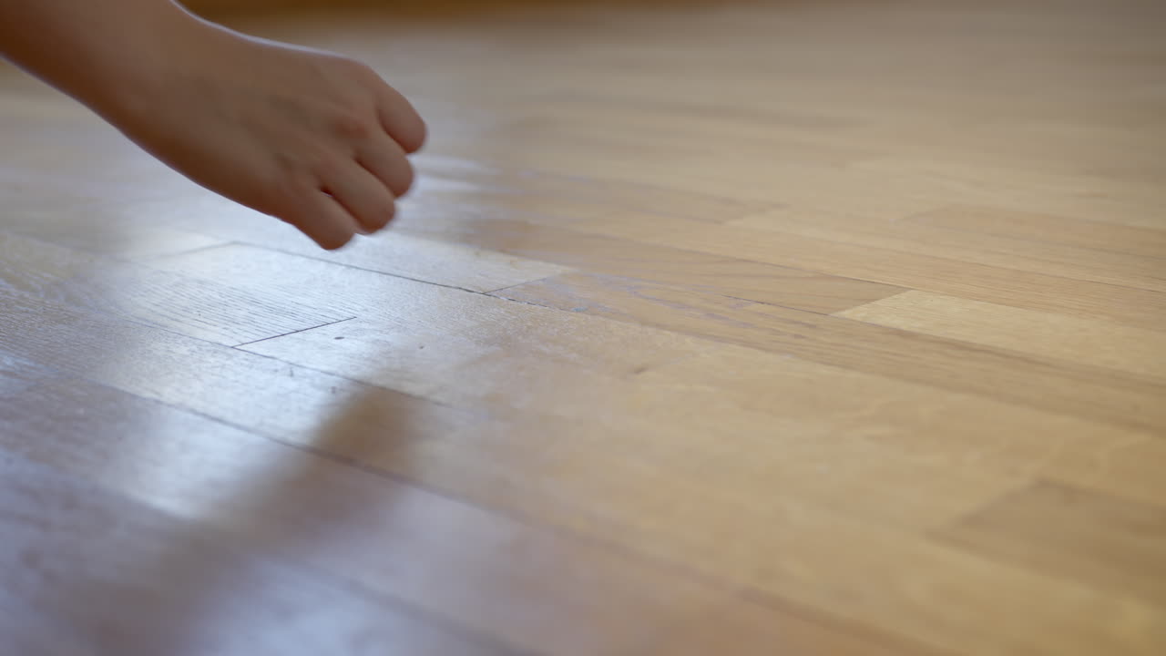 Female hand picking up plastic scraps from wooden floor of empty apartment. Close up
