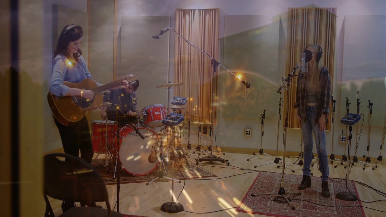 Inicio de grabación en estudio, guitarrista rasgueando, baterista tocando, vocalista cantando, con una superposición de chispas cálidas.