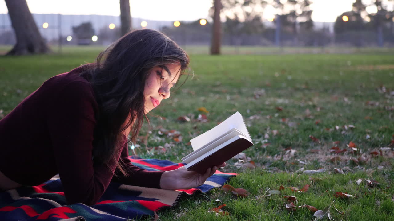 una joven hispana leyendo un libro y relajándose en el parque al atardecer