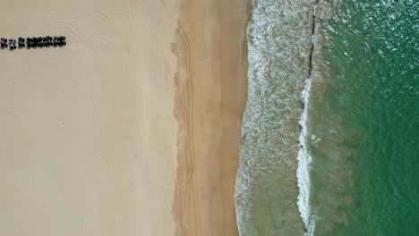 green ocean water crashes on golden sandy beach, top down aerial rising