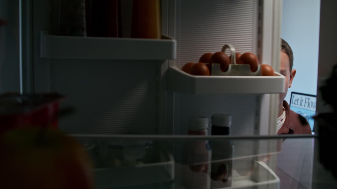 un adolescente mirando dentro de un refrigerador