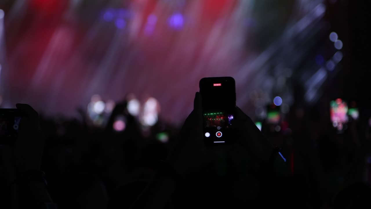 Fans recording video with smartphones at live concert, music group performing on stage