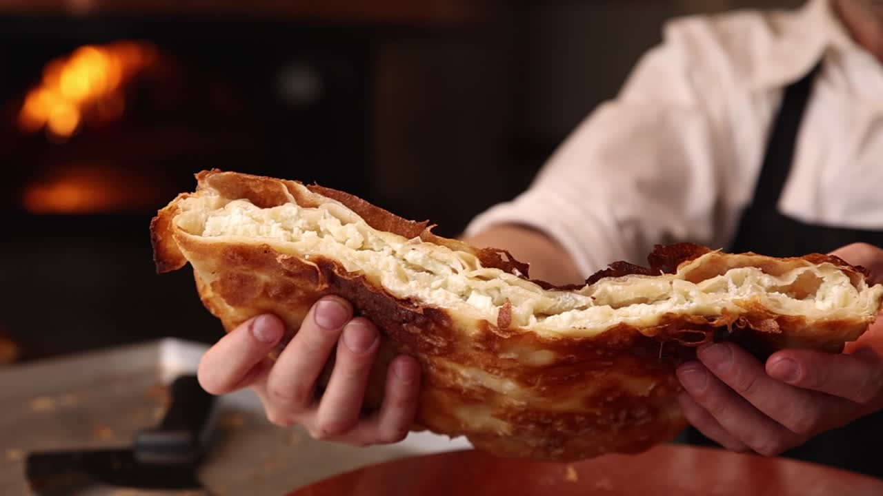 Mani che tengono un prodotto da forno al formaggio appena sfornato da un forno a legna