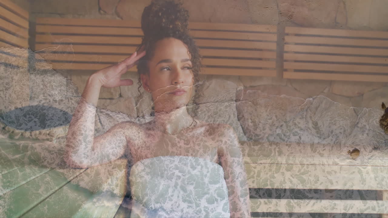 Animation of sea lapping on beach over happy biracial woman relaxing in sauna