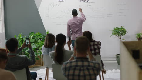 Gente-De-Negocios-Reuniéndose-Con-Un-Hombre-De-Negocios-Profesional-Que-Presenta-Un-Seminario-De-Capacitación-Financiera-Que-Muestra-Una-Estrategia-De-Marketing-Exitosa.-Estudiantes-Que-Usan-Un-Teléfono-Inteligente-Para-Grabar-Presentaciones-Y-Compartir-En-Línea.