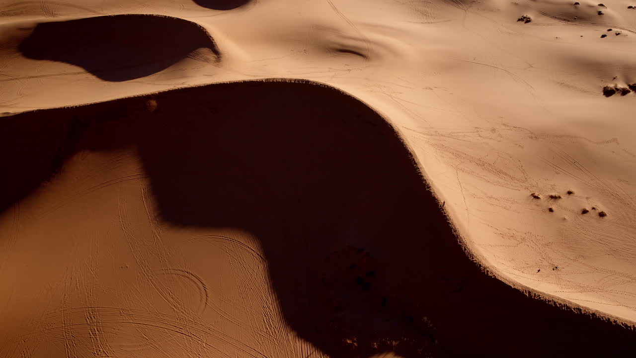 A dramatic drone shot captures the vibrant pink sand dunes and their fascinating land features.
