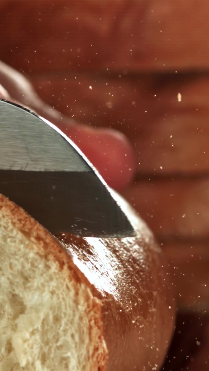 Close-up of a Serrated Knife Slicing Freshly Baked Bread with Crumbs Flying