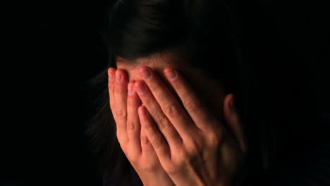 upset brunette with her head in her hands on black background