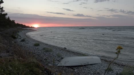 Baltic-seashore-during-sunset,-waves-hitting-the-rocky-beach-with-a-small-rowboat-in-the-corner-of-the-frame