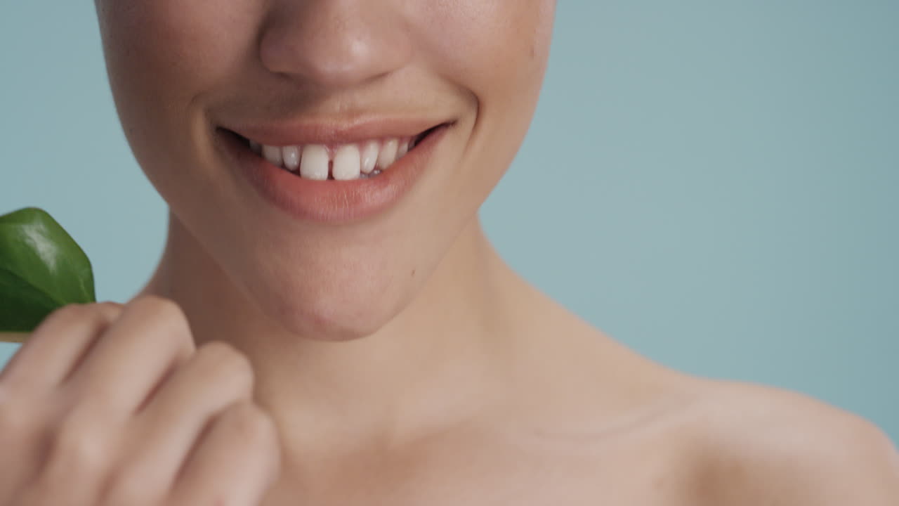 가까운 초상화 섹시한 젊은 여성 잎으로 얼굴을 만지며 부드러운 건강한 피부 피부색을 즐기며 파란색 배경의 자연적인 아름다움을 즐기고 피부 관리 개념