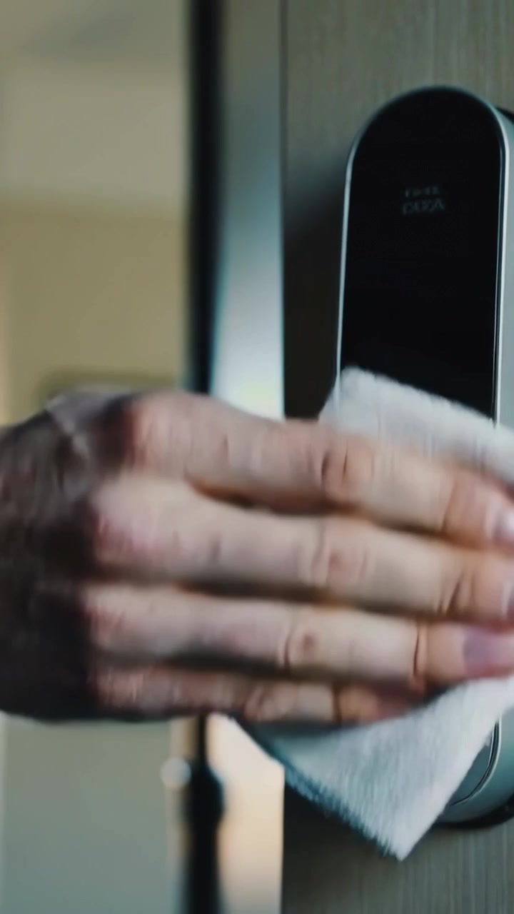 Video verticale: Mano adulta che pulisce il display di una serratura intelligente e il buco della serratura su una porta di legno con un panno