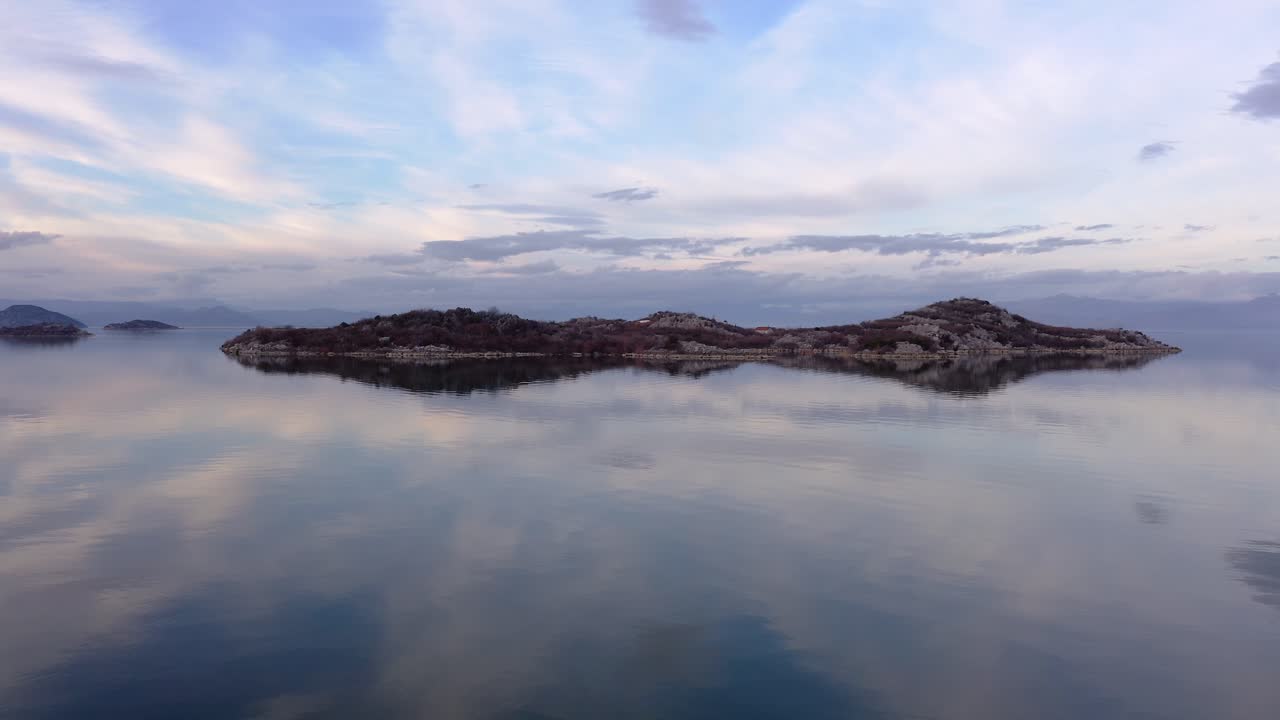 맑은 물이 흐린 하늘과 아름다운 녹색 섬을 가운데에 반영하는 스카다르 호수의 느린 동작