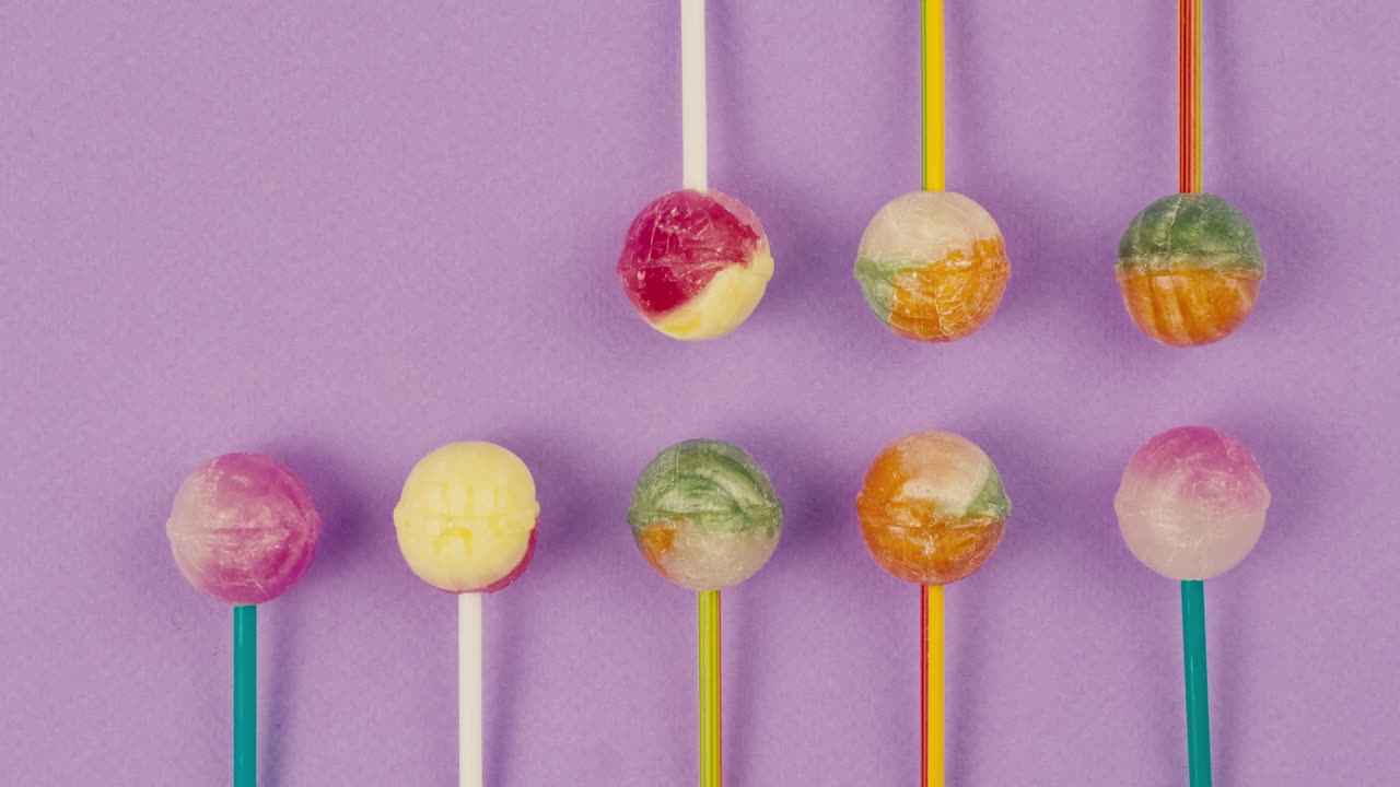 Sweet lollipops appear on color purple background. Bright texture sugar candies close up top view. Composition of favorite children's summer sweets. Studio shot for shop, supermarket, confectionery