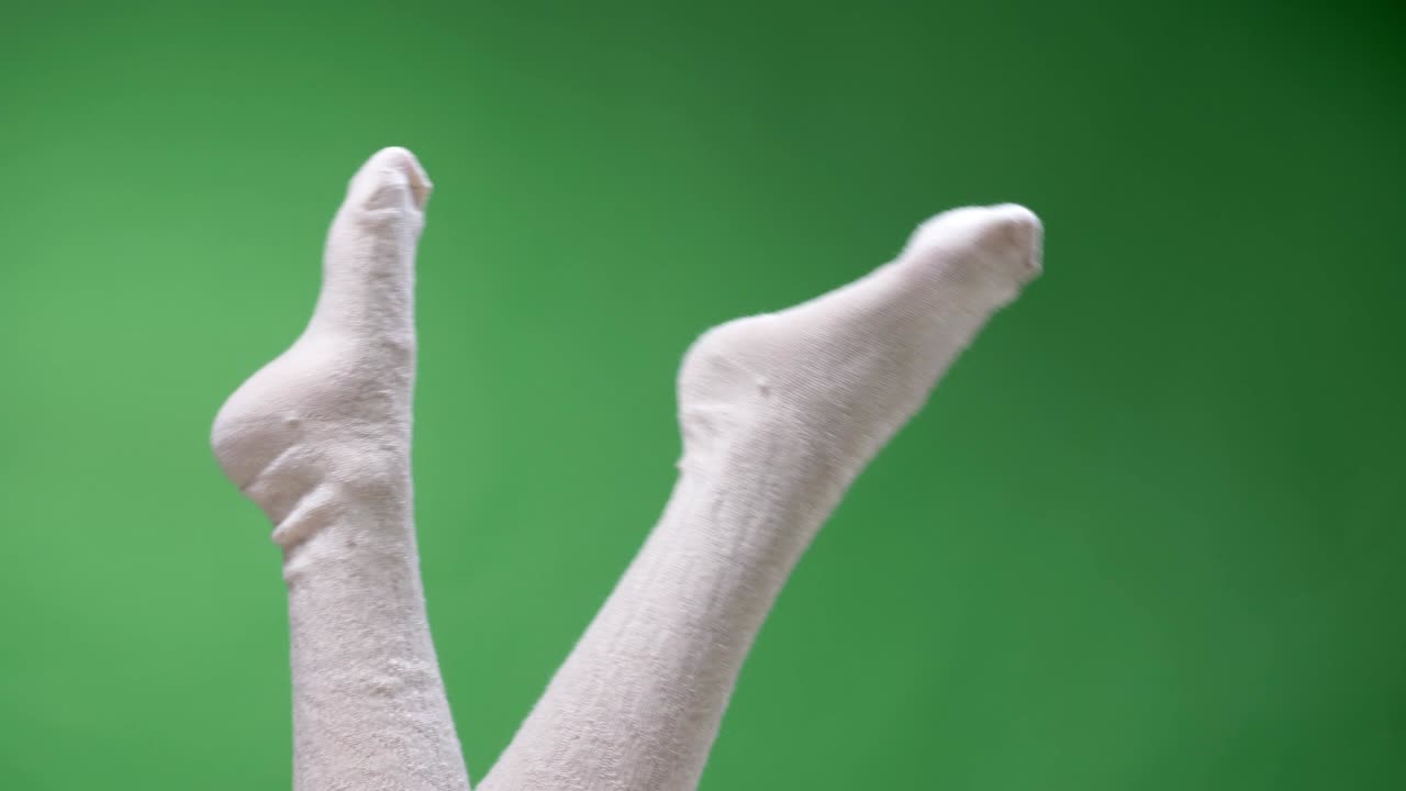 primer plano de los pies superiores disparar de las piernas de la adolescente femenina en lindos calcetines blancos de rodilla jugoso moviéndose con el fondo aislado en verde