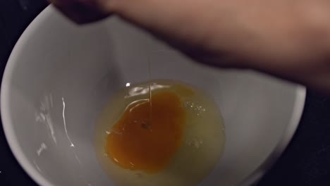 Static-close-up,-person's-hand-cracking-single-egg-into-bowl,-slow-motion