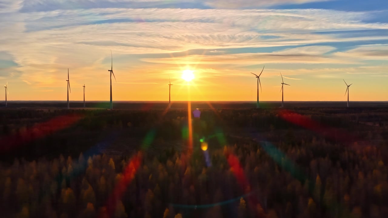 Luftfoto af vindmøller ved solnedgang med glødende horisont over fladt landligt landskab, drone