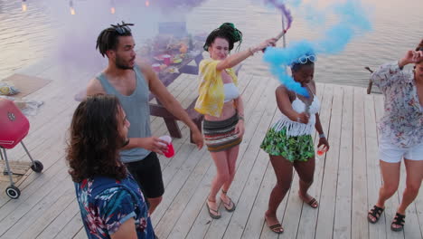 friends having party and dancing with smoke bombs on pier