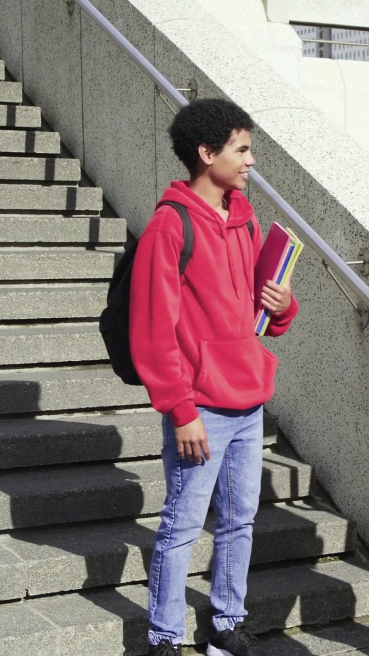 Video verticale: Adulto si avvicina e abbraccia uno studente sui gradini del campus, offrendo uno smartphone, con spazio per il testo