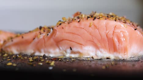 Delicious-thick-piece-of-pink-salmon-sushi-sizzling-and-cooking-with-speckled-spices,-close-up-static-side-view