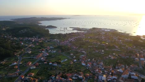 Vuelo-Aéreo-Sobre-El-Pueblo-De-O-Grove-En-Galicia-Durante-La-Puesta-De-Sol-Hacia-La-Bahía-Con-Granjas-De-Mejillones-En-La-Distancia