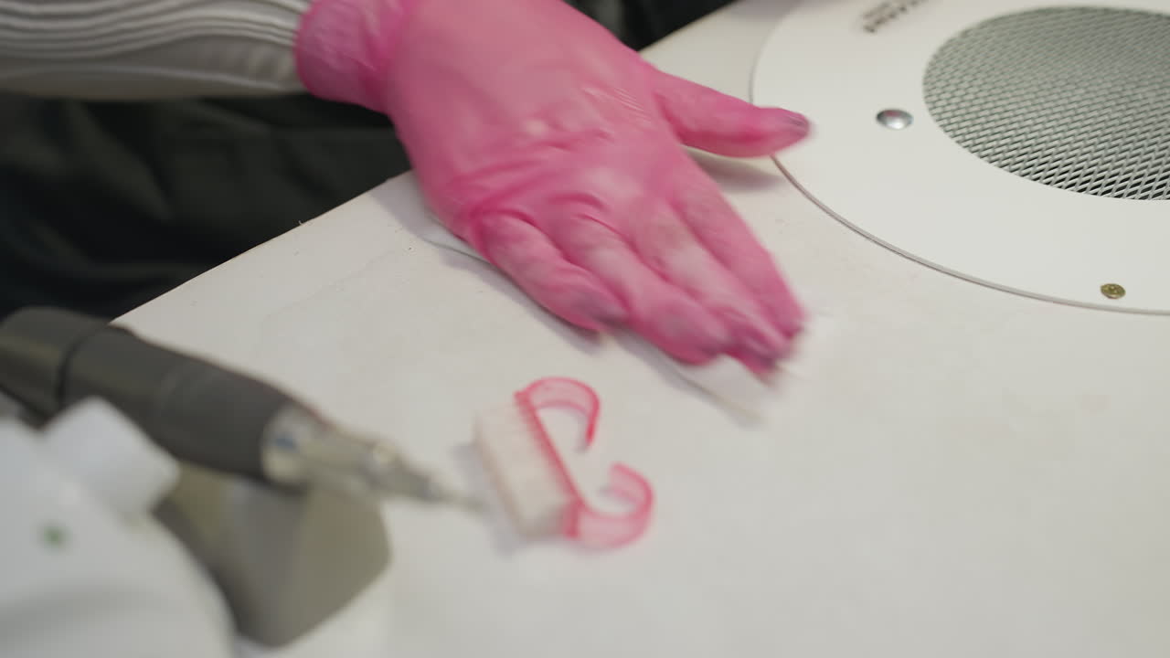 Closeup of nail technician cleaning manicure table after session with orange stick, nail brush, and drill tool in view, highlighting neat work area and attention to hygiene in professional salon