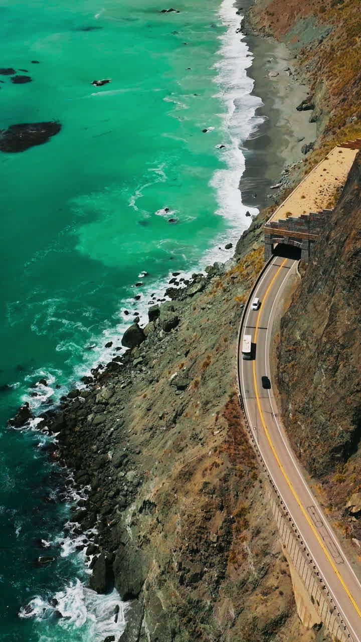 Dangerous road coming by the middle of the mountain. Stunning view of the azure Pacific ocean meeting rocky coastline. Aerial perspective. Vertical video