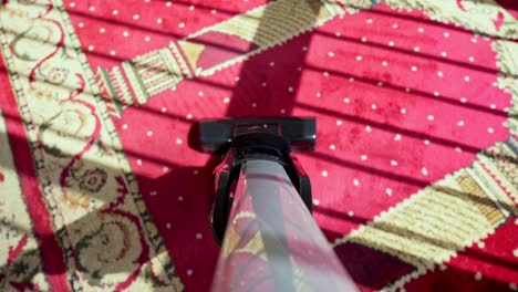 close-up of vacuuming a vibrant red islamic prayer rug with intricate patterns. morning sunlight casts shadows. ideal for cleaning, culture, routine, or faith-themed content.