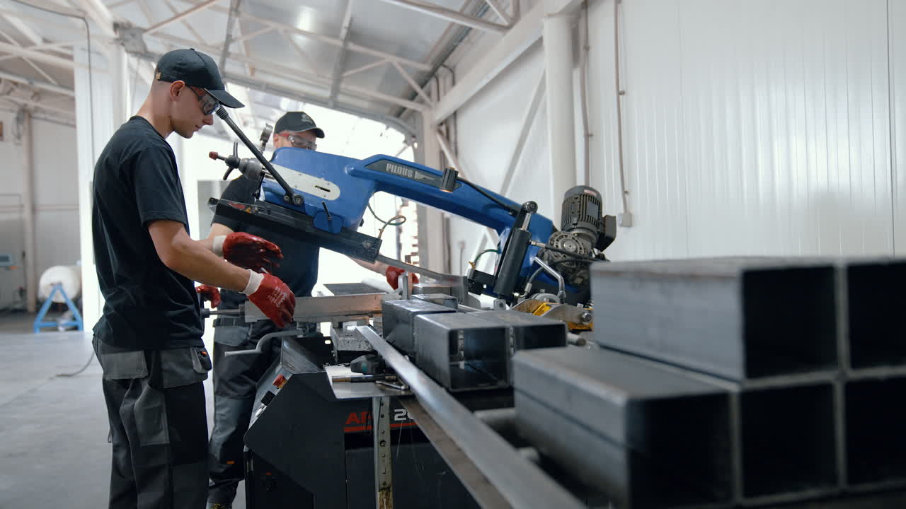 VINNYTSIA, UKRAINE - JANUARY 19, 2023: Workers in uniform wearing gloves and safety glasses work at machine with metal products in factory