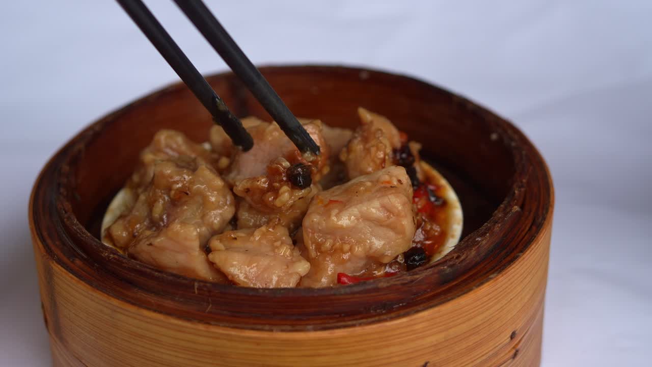 Close up shot of a traditional dim sum dish, featuring pork ribs in black bean sauce, served in bamboo steamer at the restaurant, picked up with chopsticks.