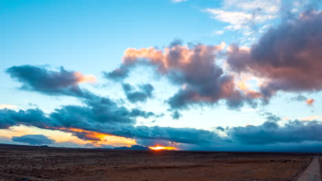 Colorful-golden-sunset-over-the-barren-Mojave-Desert-landscape-with-dynamic-wind-shears-pushing-cloud-layers-in-different-directions---sliding-aerial-hyper-lapse