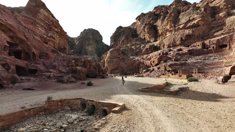 Aerial-view-following-people-riding-through-a-desert-canyon-in-Petra,-Jordania