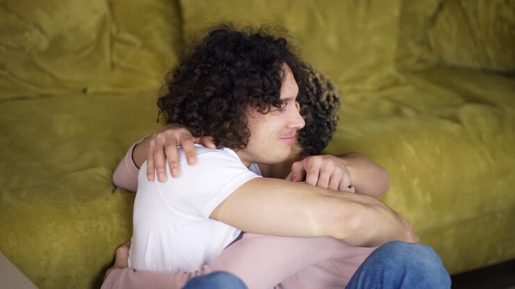 Giovane coppia gay felice seduta tra scatoloni di cartone con le chiavi della loro nuova casa.