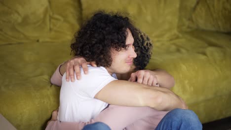 happy young gay couple sitting amongst cardboard boxes with keys of their new house