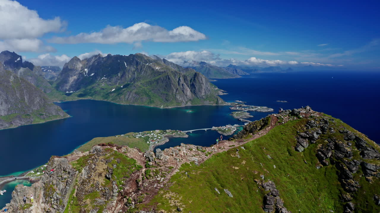 Aerial drone shot over Reinebringen, Reine, Lofoten Islands, Norway.
High view of the picturesque green landscape. View of the fjords and blue nordic sea. Touristic attraction for hiking activities.