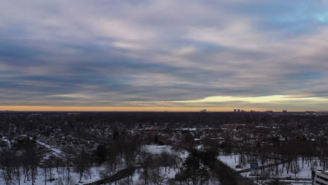 An-aerial-shot-over-a-suburban-neighborhood-during-a-cloudy-but-golden-sunrise,-taken-after-a-snow-storm